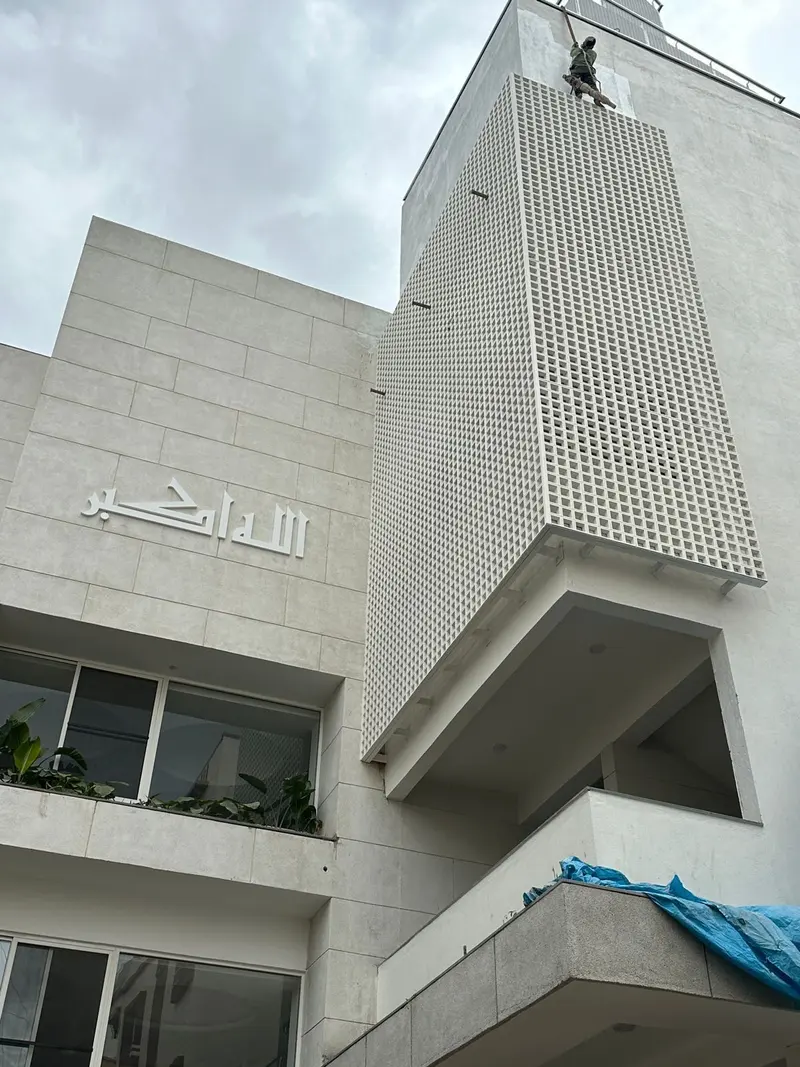 Square-grid jali screen on the projecting front of Bismilla Green Masjid, with calligraphy on the facade
